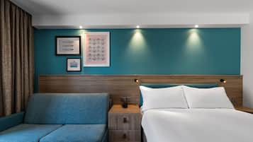 A hotel room with a bed, a sofa, and two wall-mounted lights.