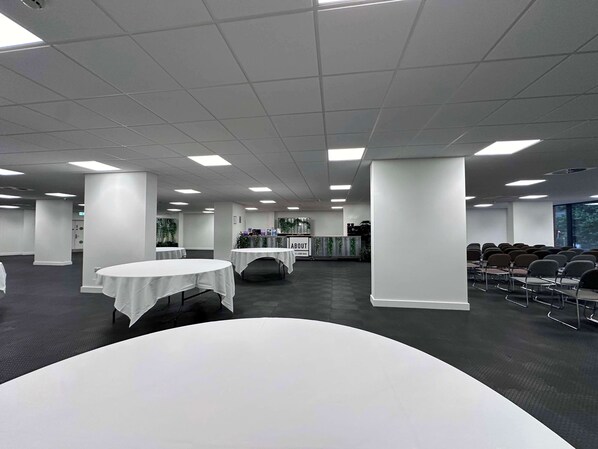 A spacious conference room with white tables, a long table, and rows of chairs.