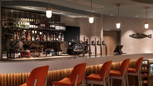 A bar area with multiple stools, a bar counter, and a variety of bottles and glasses. - Hampton by Hilton Torquay (Torquay)