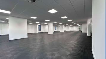 A spacious, empty office with a grid of ceiling lights, dark carpeting, and white walls.