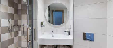 A modern bathroom with a glass shower enclosure, a white sink with a mirror above, and a blue door in the background.