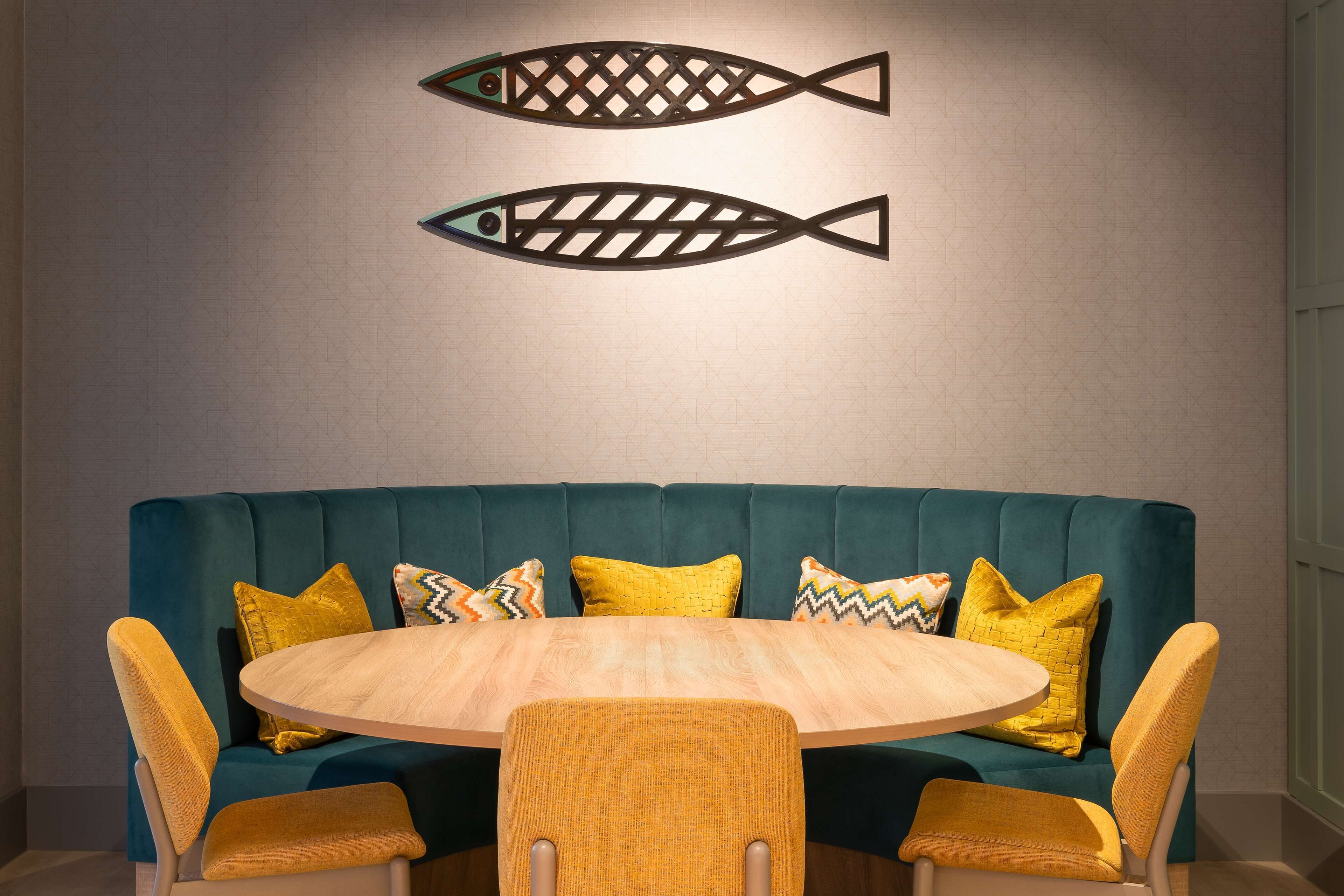 Un canapé de couleur bleu-vert avec des coussins jaunes, une table ronde en bois et deux décorations murales représentant des poissons.