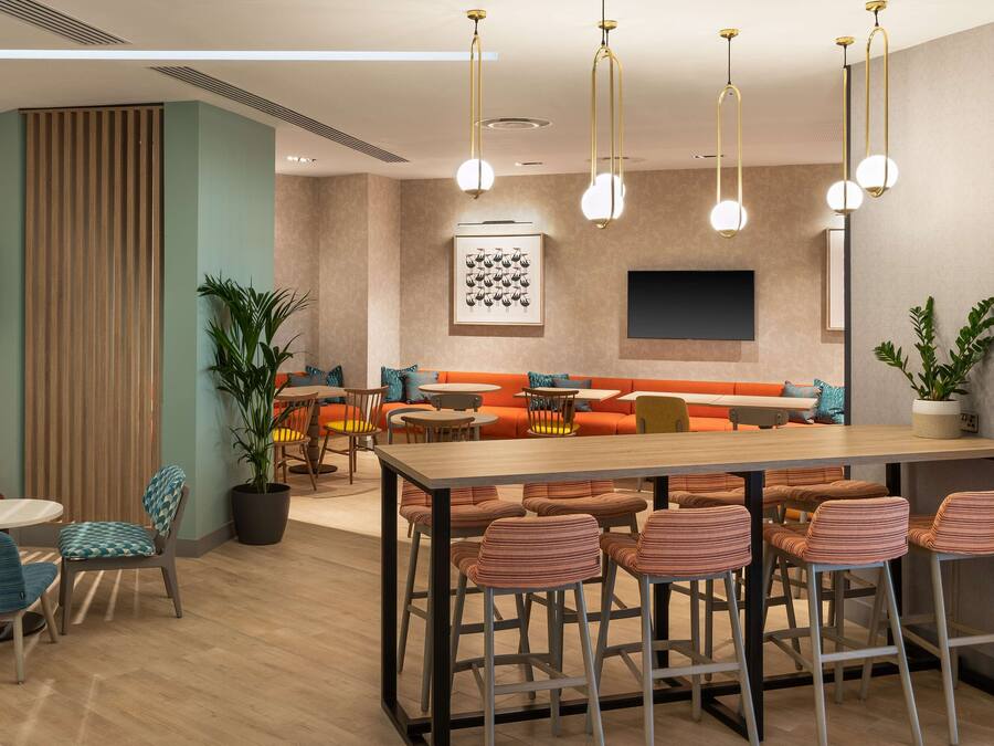 A modern lounge area with a long table, bar stools, and a sofa.