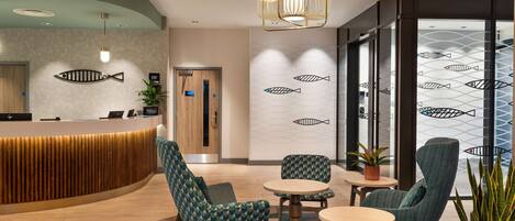 A modern reception area with a curved wooden reception desk, teal patterned chairs, and a round table.