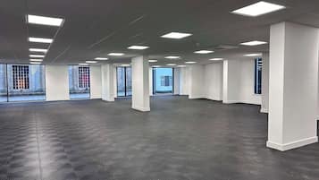 A spacious, empty office with a grid of ceiling lights, large windows, and a patterned floor.