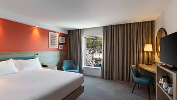 Habitación de hotel con cama, escritorio, silla, televisión y ventana con cortinas.