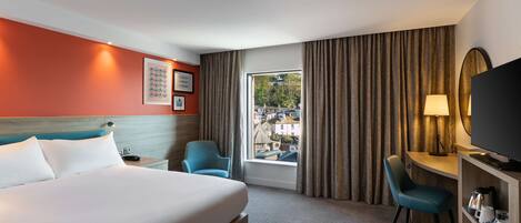 A hotel room with a bed, a desk, a chair, a TV, and a window with curtains.