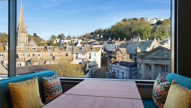 A room with a large window overlooking a town with historic buildings and a church spire. - Hampton by Hilton Torquay (Torquay)