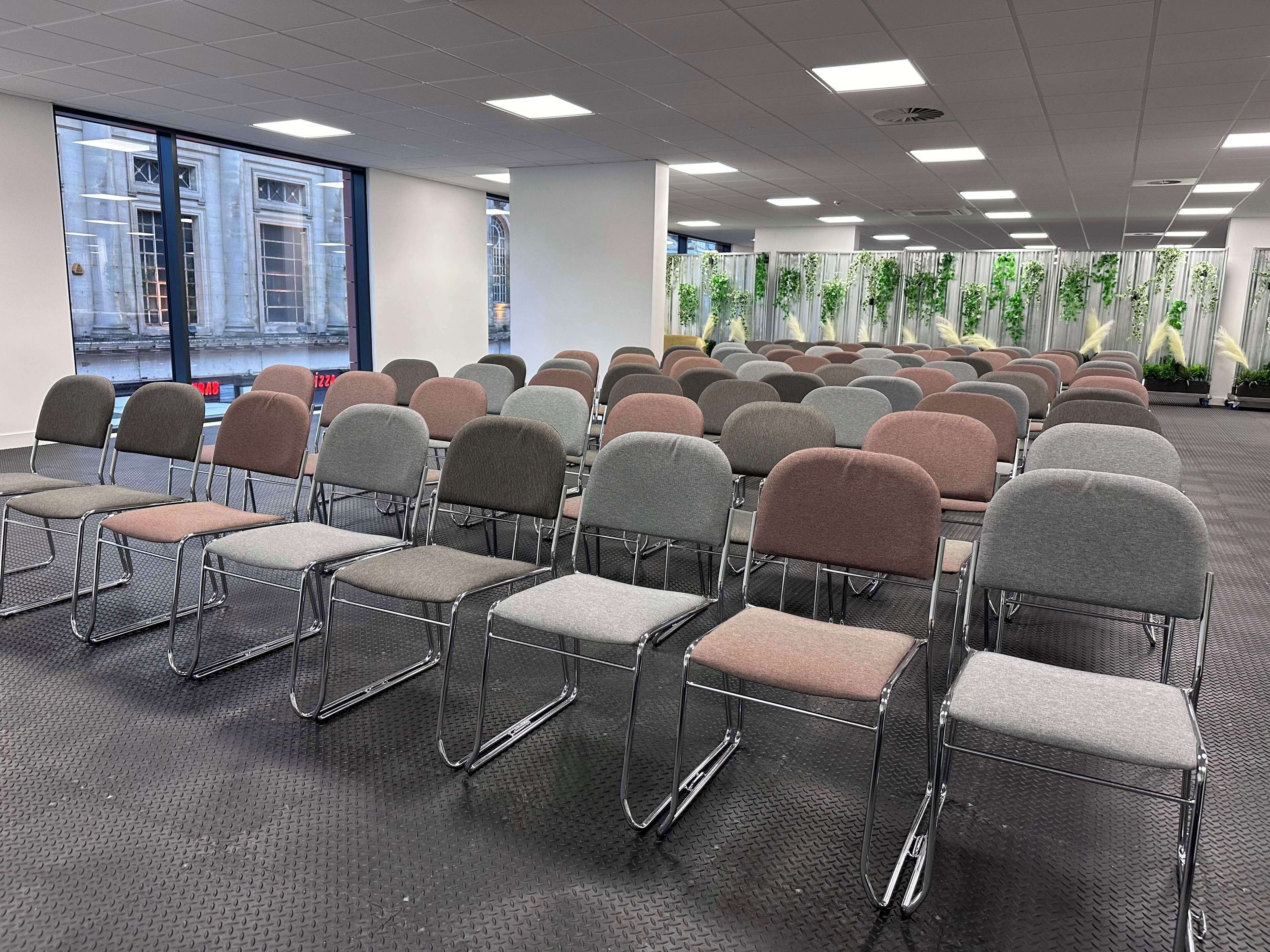 A conference room with rows of metal-framed chairs and a large window with a city view.