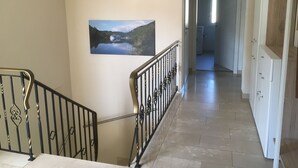 A hallway with a staircase, a painting of a lake, and a door leading to another room. - Newly renovated (in 2020) vacation apartment, 4 p., with a great view of the Moselle valley (Briedern)