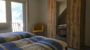 A bedroom with two beds, a yellow chair, and a wooden wardrobe. - Newly renovated (in 2020) vacation apartment, 4 p., with a great view of the Moselle valley (Briedern)