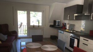 A compact living space with a kitchenette, a dining area with a table and chairs, a sofa, and a view of the outdoors. - Newly renovated (in 2020) vacation apartment, 4 p., with a great view of the Moselle valley (Briedern)