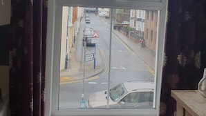 Una ventana con vista a una calle, un cartel de cine y un letrero de advertencia triangular.