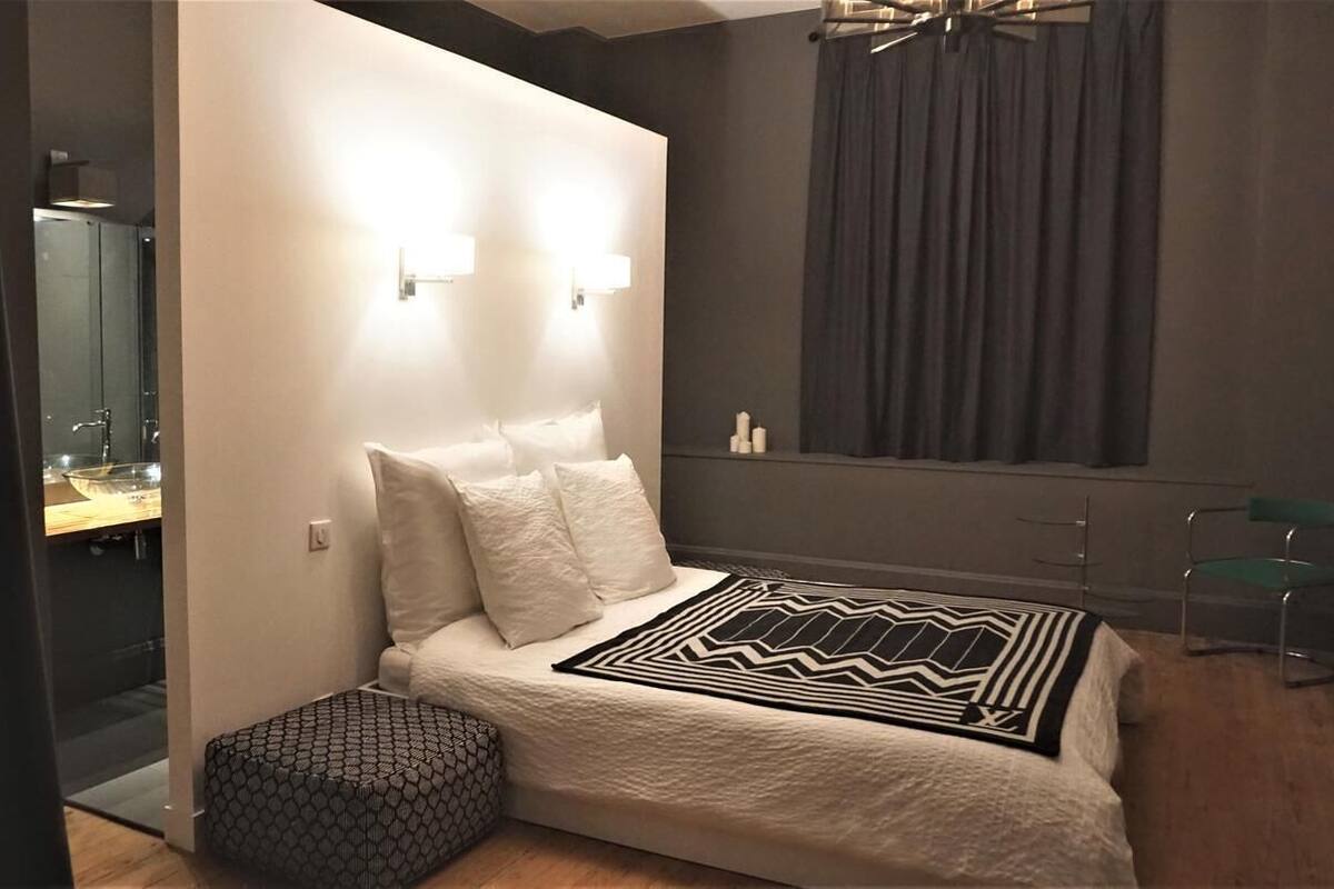 A modern bedroom with a large bed, a bedside table, a mirror, and a window with curtains.