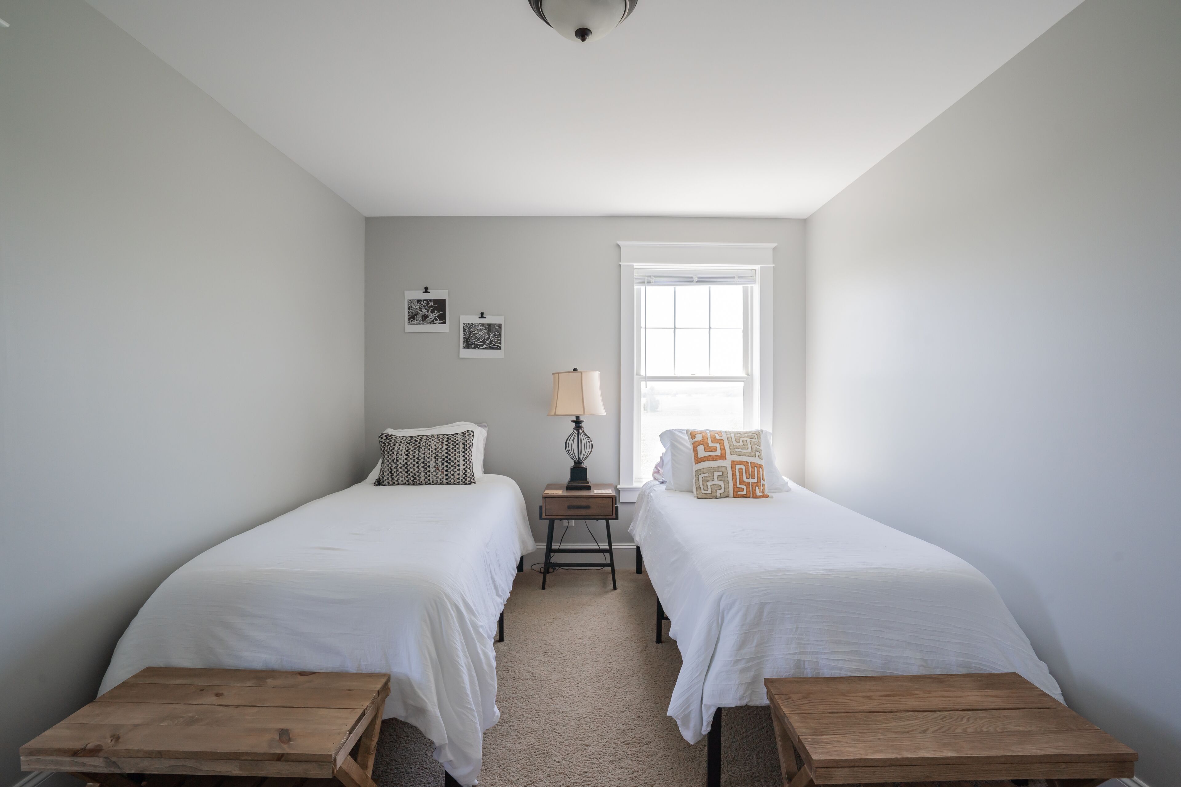 Quarto com duas camas, mesa de cabeceira, abajur e janela.