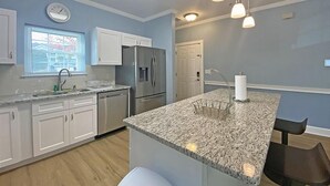A modern kitchen with white cabinets, a granite countertop, stainless steel appliances, and pendant lighting. - Magnolia Place by Palmetto Vacations (Myrtle Beach)
