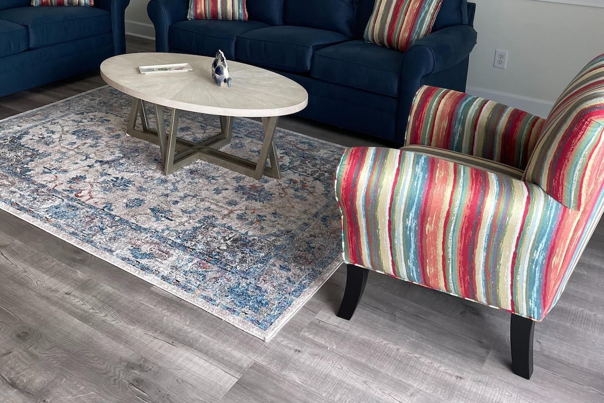 Ein Wohnzimmer mit blauem Sofa, einem runden Couchtisch und einem farbenfrohen Streifenstuhl.