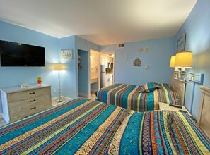 Een slaapkamer met twee bedden, een dressoir, een televisie en een badkamer zichtbaar door een geopende deur.