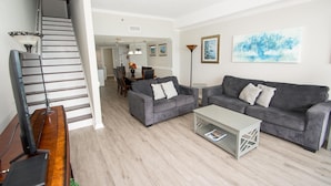 A living room with a staircase, grey sofas, a coffee table, and a dining area in the background. - Ocean Forest 2309 (Myrtle Beach)