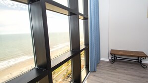 A room with large windows overlooking a beach, a wooden bench, and a blue curtain. - Ocean Forest 2309 (Myrtle Beach)