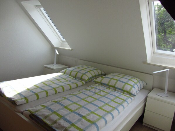 Une chambre à coucher comprenant un lit, deux tables de chevet, une fenêtre et un puits de lumière.