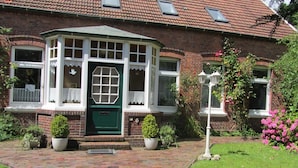 A brick house with a green front door, white window frames, and a small porch. - Bright charming apartment with garden, terrace, WLAN  (Niedersachsen - Dornum)