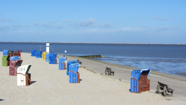 A beach with numbered beach huts and a pier extending into the water. - Bright charming apartment with garden, terrace, WLAN  (Niedersachsen - Dornum)