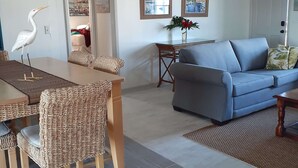 A spacious living area with a dining table, wicker chairs, a blue sofa, and a dining table with a vase of flowers. - Heron Cottage - Private & Quaint (Panama City)