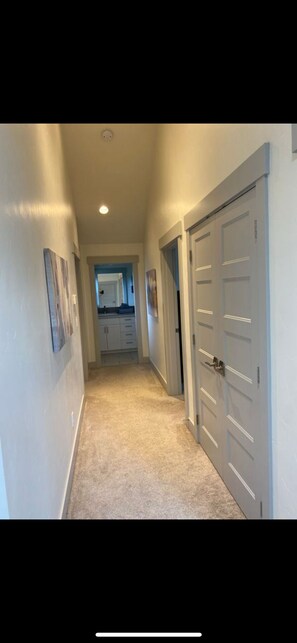 A hallway with a carpeted floor, white walls, and a door on the right.
