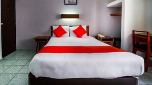 Habitación de hotel con una cama grande, dos mesitas de noche, una silla de madera, una lámpara de pared y un cuadro sobre la cama.
