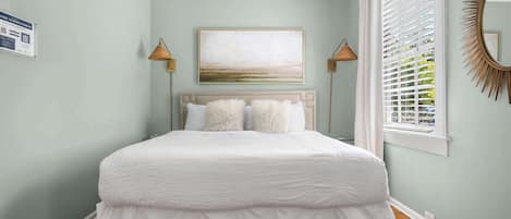 Un dormitorio con una cama grande, un cuadro encima y una ventana con persianas.