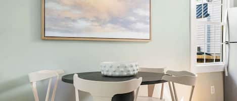 A dining area with a round table, four chairs, and a large painting on the wall.
