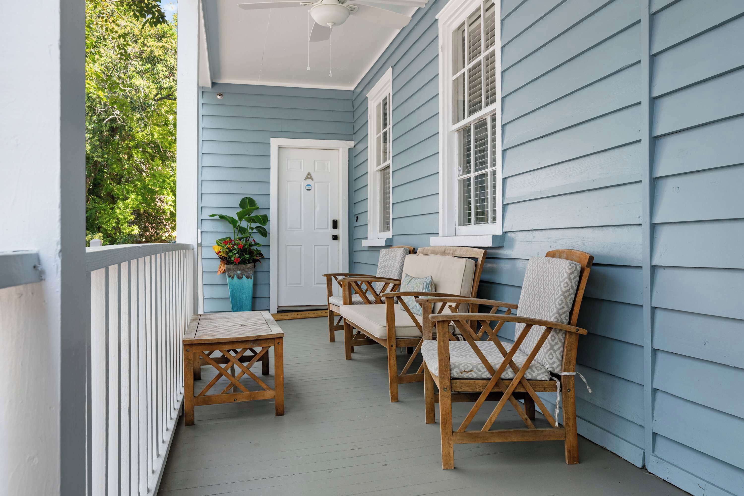 A porch with a white door, two wooden chairs, a small table, and a potted plant.