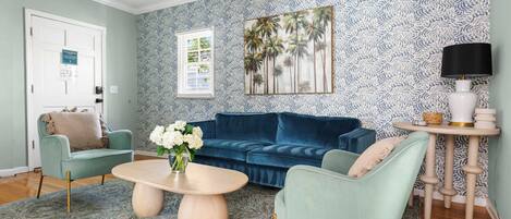 Un salón con sofá azul, una mesita de centro redonda y papel tapiz estampado.