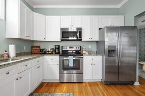 Une cuisine moderne avec des meubles blancs, des appareils en acier inoxydable, un four à micro-ondes, un four et un réfrigérateur.