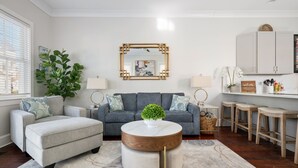 A modern living room with a grey sofa, a round coffee table with a wooden top, and a large potted plant. - Rooftop Patio, Unparalleled Views in 3-story Home (Charleston)