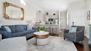 A modern living room with a sofa, armchair, and round coffee table. A kitchen is visible in the background with a microwave and refrigerator. - Rooftop Patio, Unparalleled Views in 3-story Home (Charleston)