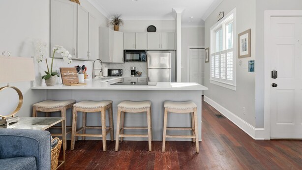 A modern kitchen with white cabinetry, a central island with stools, a refrigerator, and a microwave. - Rooftop Patio, Unparalleled Views in 3-story Home (Charleston)