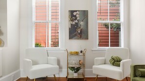 Une pièce avec deux fauteuils blancs, une étagère en fil de fer doré où sont disposés des objets en verre, et un tableau représentant des fleurs accroché au mur.