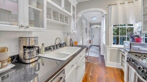 A modern kitchen with white cabinetry, a stainless steel coffee maker, and a wooden floor.