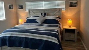 A bedroom with a bed, two bedside tables with lamps, a headboard, and two wall-mounted picture frames. - Totally Beachin! - One Block from beach - Unit 1101 - Island Dunes Condo's (Port Aransas)