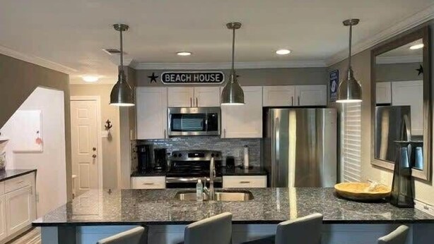 A modern kitchen with a central island, stainless steel appliances, and pendant lighting. - Totally Beachin! - One Block from beach - Unit 1101 - Island Dunes Condo's (Port Aransas)