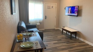 A dining area with a table set for two, a sofa, and a TV mounted on the wall displaying a news program. - Newer private apart-hotel suite in Old Town (San Diego)