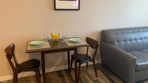 A dining area with a table set for two, two chairs, a glass bowl of lemons, and two wine glasses. A framed picture hangs on the wall above the table. - Newer private apart-hotel suite in Old Town (San Diego)
