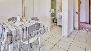 En matplats med ett bord dukat för två personer, en vit vägg med ett färgstarkt konstverk och utsikt över ett badrum med en grön vägg och vita sanitetsartiklar.