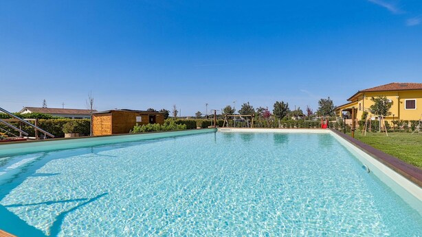 En pool med klart vatten och en träbrygga runt om, omgiven av en välskött gräsmatta och några få byggnader.