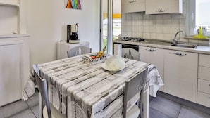 A compact kitchen with a dining area, featuring a coffee machine, a dishwasher, and a window with a view.