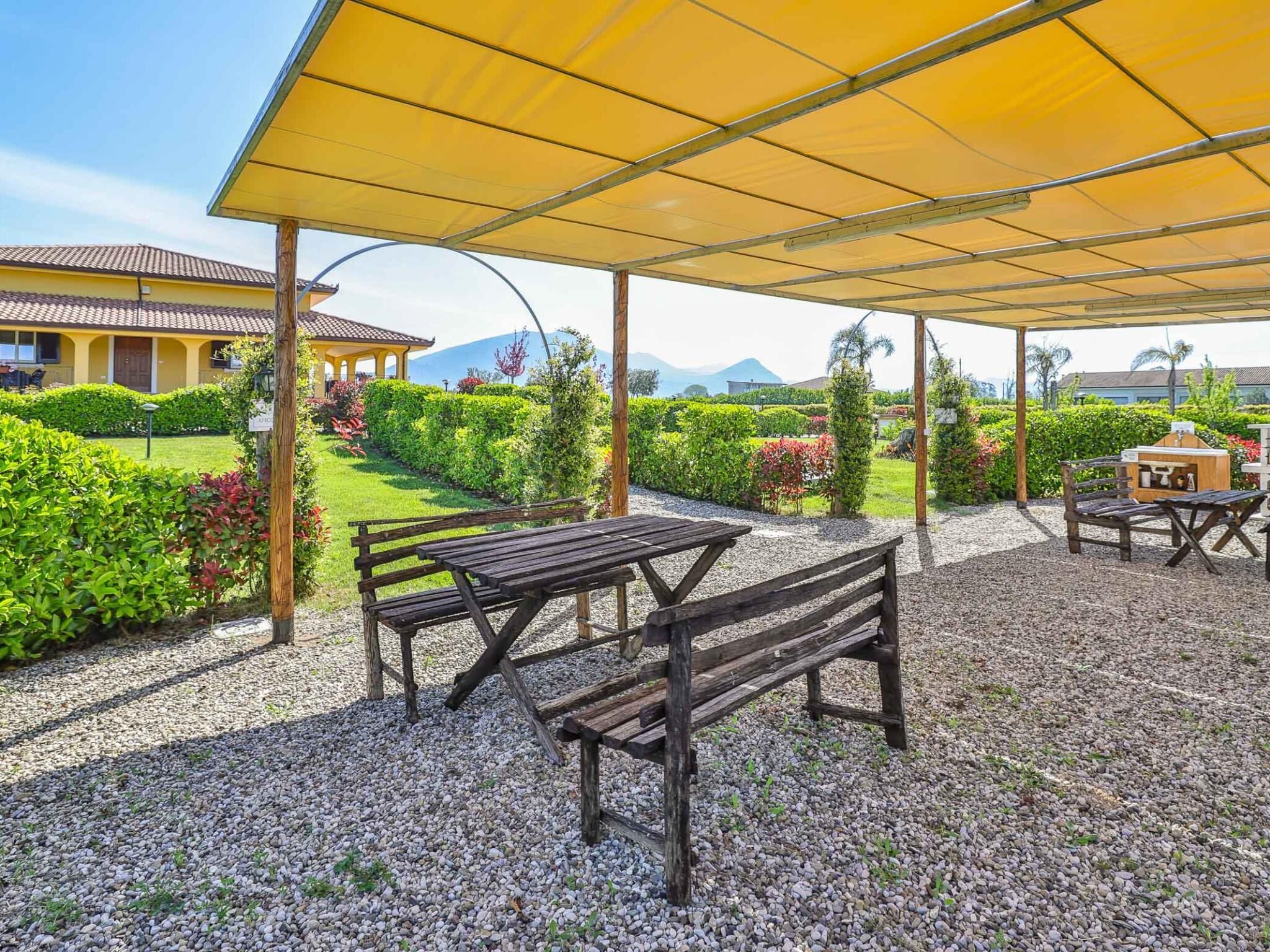 Eine Außenpatio mit Holzbänken und Tischen, einer Grillgegend und einem gelben Sonnensegel.