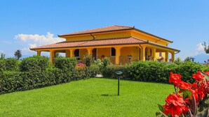 Uma vila amarela com telhado em cerâmica, rodeada por um jardim e relvado bem cuidados.