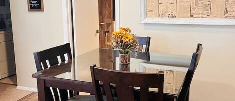 Un comedor con una mesa y sillas de madera, un florero con flores y un periódico enmarcado en la pared.